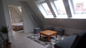 Quarto de loft moderno com teto inclinado, claraboias, uma mesa de madeira, um sofá escuro e um tapete estampado.