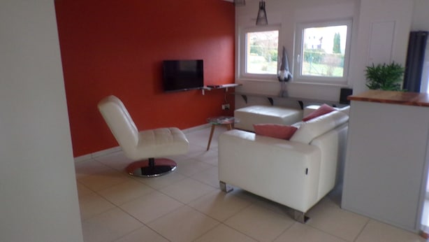 Uma sala de estar moderna com uma parede em destaque vermelha, um sofá branco, uma poltrona branca e uma TV de tela plana fixada na parede.