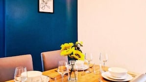 Zona pranzo con tavolo in legno apparecchiato per quattro persone, pareti blu e lampade a sospensione.