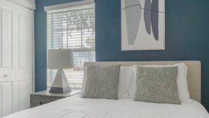 A bedroom with a bed, a nightstand, a lamp, and a window with blinds. - Landing | Stylish 2BD, Gym (Dunedin)