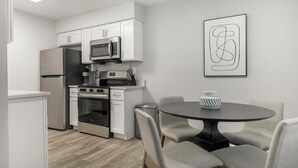 A modern kitchen with white cabinetry, stainless steel appliances, and a dining area with a round table and chairs. - Landing | Stylish 2BD, Gym (Dunedin)