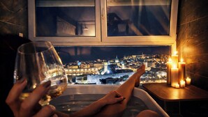 A bathtub with a city view, candles, and a glass of wine.