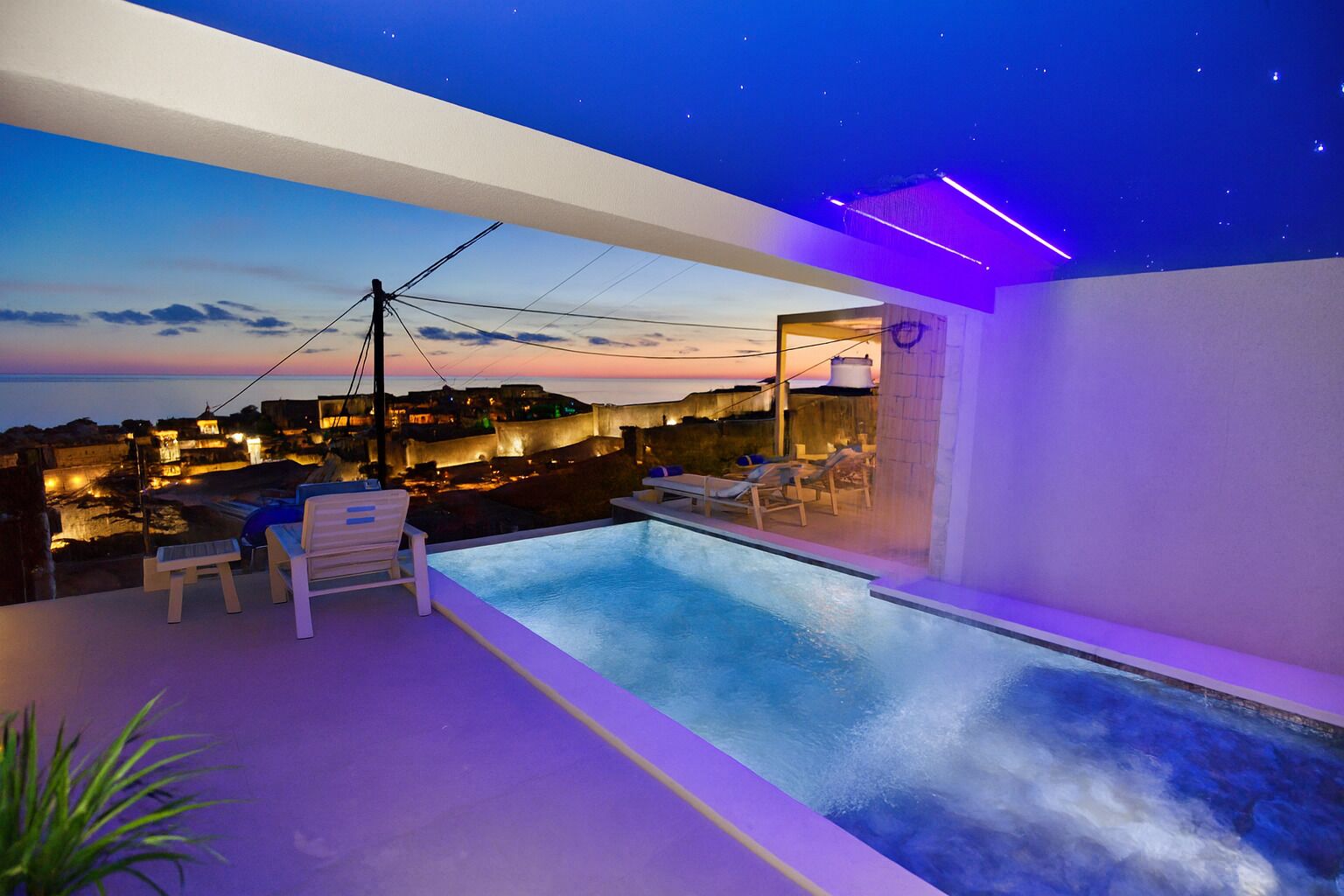A rooftop infinity pool with lounge chairs and a city view at dusk.