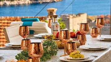 A table set with copper wine glasses, plates, and a bottle, with a scenic coastal view in the background.