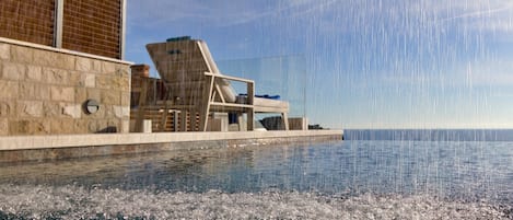 A poolside area with a clear view of the sea, a lounge chair, and a building with a tiled facade.