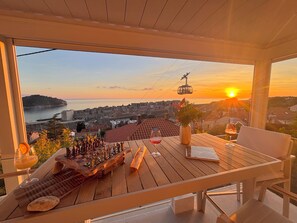 A wooden table with chess set, wine glasses, and a book, overlooking a coastal cityscape with a sunset. - Villa D’ Republic Dubrovnik – Infinity Pool & Old Town Views (Dubrovnik)