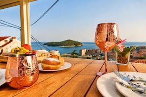 A table with a copper mug, a glass of drink, pastries, and a view of the sea.