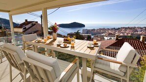 A terrace with a table set for breakfast, overlooking a coastal city and the sea.