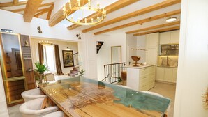 A spacious dining area with a long wooden table and chairs, a glass-top table, and a chandelier.