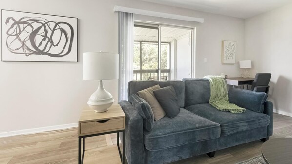 Ein modernes Wohnzimmer mit grauem Sofa, einer weißen Lampe und einem großen abstrakten Gemälde an der Wand.