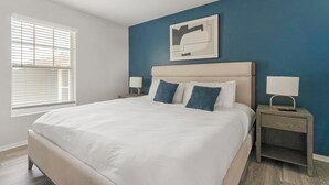 Une chambre à coucher avec un grand lit, deux tables de chevet avec des lampes, une fenêtre avec des stores et une œuvre d’art accrochée au mur.