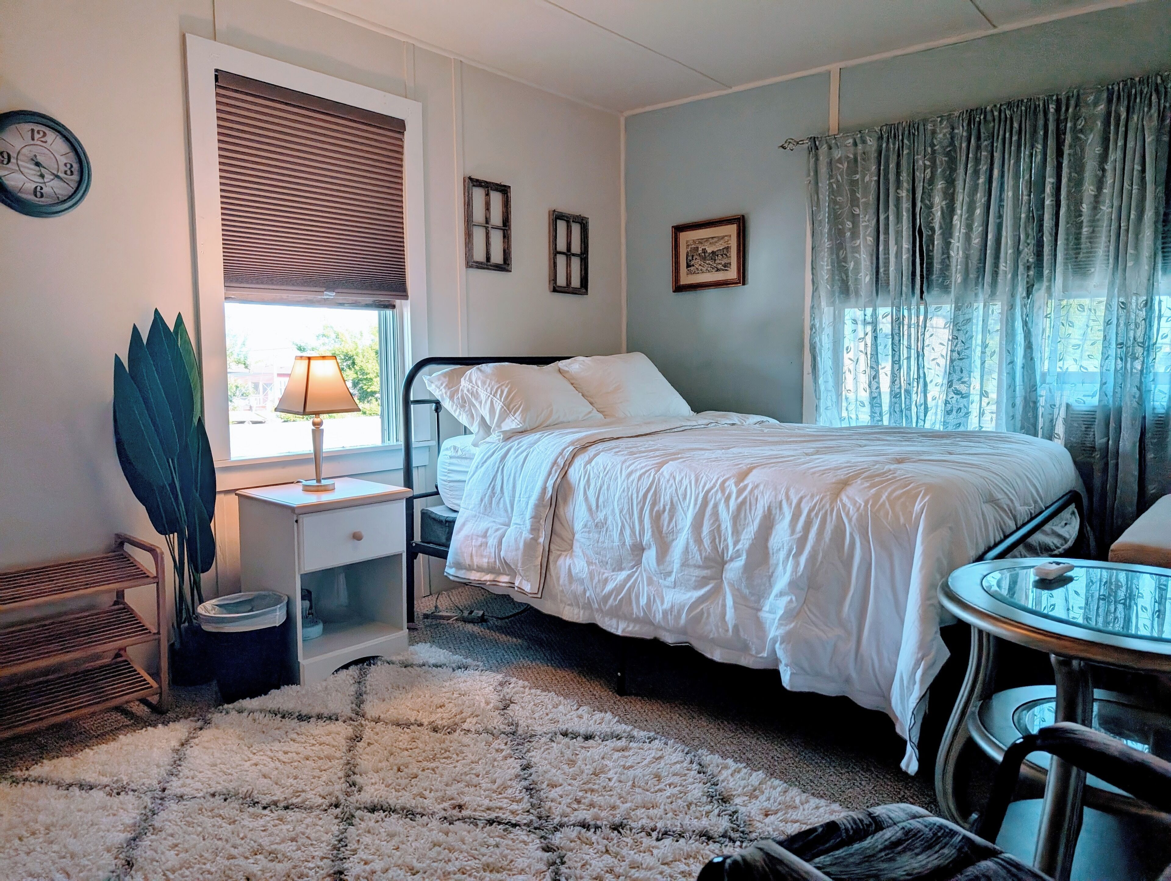 A bedroom with a bed, bedside table, lamp, chair, and a small table.