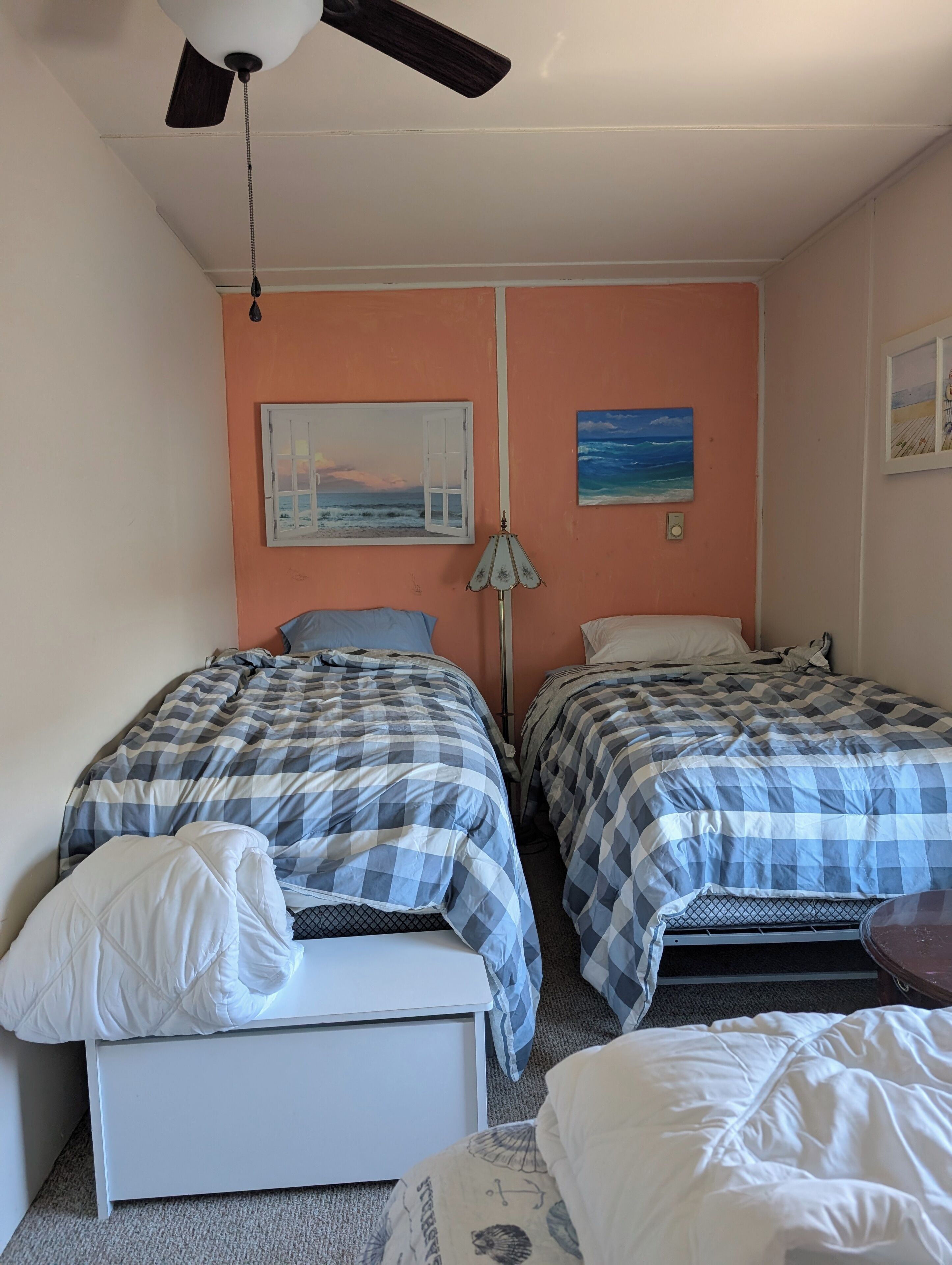 A room with two beds, a ceiling fan, a desk, and a bench.