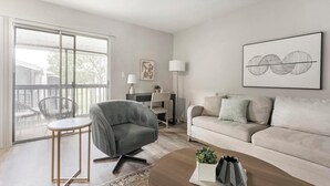 A modern living room with a grey sofa, a round coffee table, and a dining area with a chair and table. - Landing | Stylish 1BD, Gym (Dunedin)