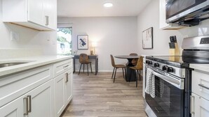 Een moderne keuken met witte kastjes, een roestvrijstalen fornuis en een eethoek met twee stoelen.