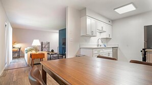 Moderni keittiö, jossa on valkoiset kaapit, ruostumattomasta teräksestä valmistettu jääkaappi sekä ruokailutila, jossa on puinen pöytä ja tuolit.