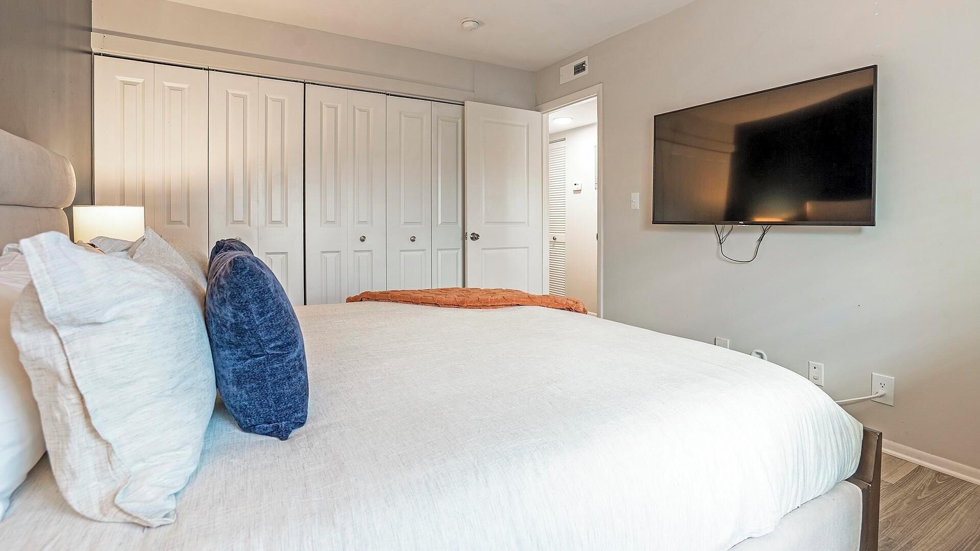 Ein Schlafzimmer mit einem großen Bett, einem an der Wand montierten Fernseher und einem Kleiderschrank mit Schiebetüren.