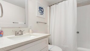 Une salle de bain moderne avec un lavabo blanc, un miroir, un rideau de douche et une œuvre d’art encadrée accrochée au mur.