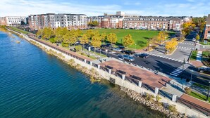 A riverside urban area with modern buildings, a pedestrian walkway, and a parking lot. - Landing | Modern 1BD, Game Room, Clubhouse (Bayonne)