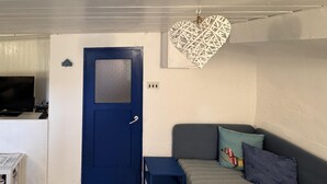 Et værelse med en blå dør, et lille bord, en sofa med puder og en hjerteformet dekoration på væggen.