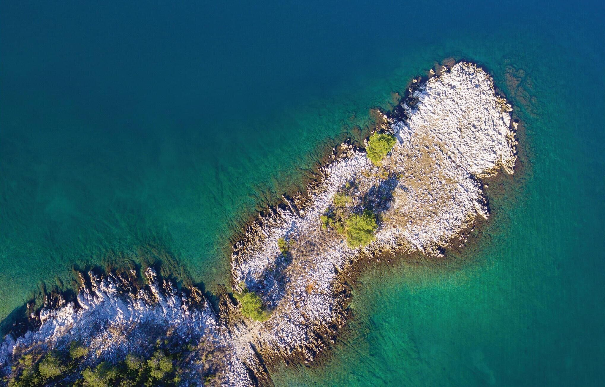 An aerial view of a coastal area with rocky terrain and clear blue waters.