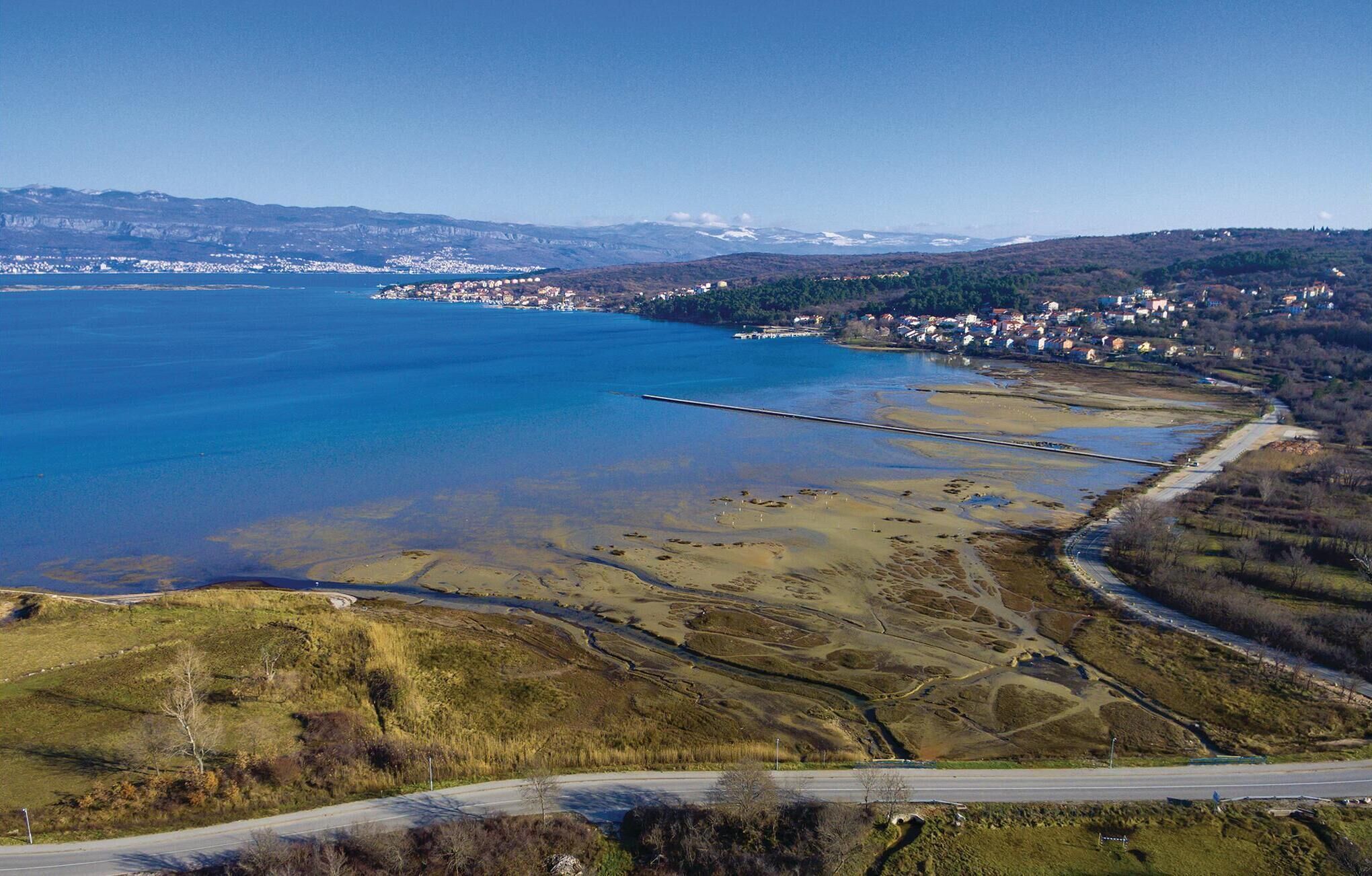 An aerial view of a coastal area with a clear road, a large body of water, and a distant town.