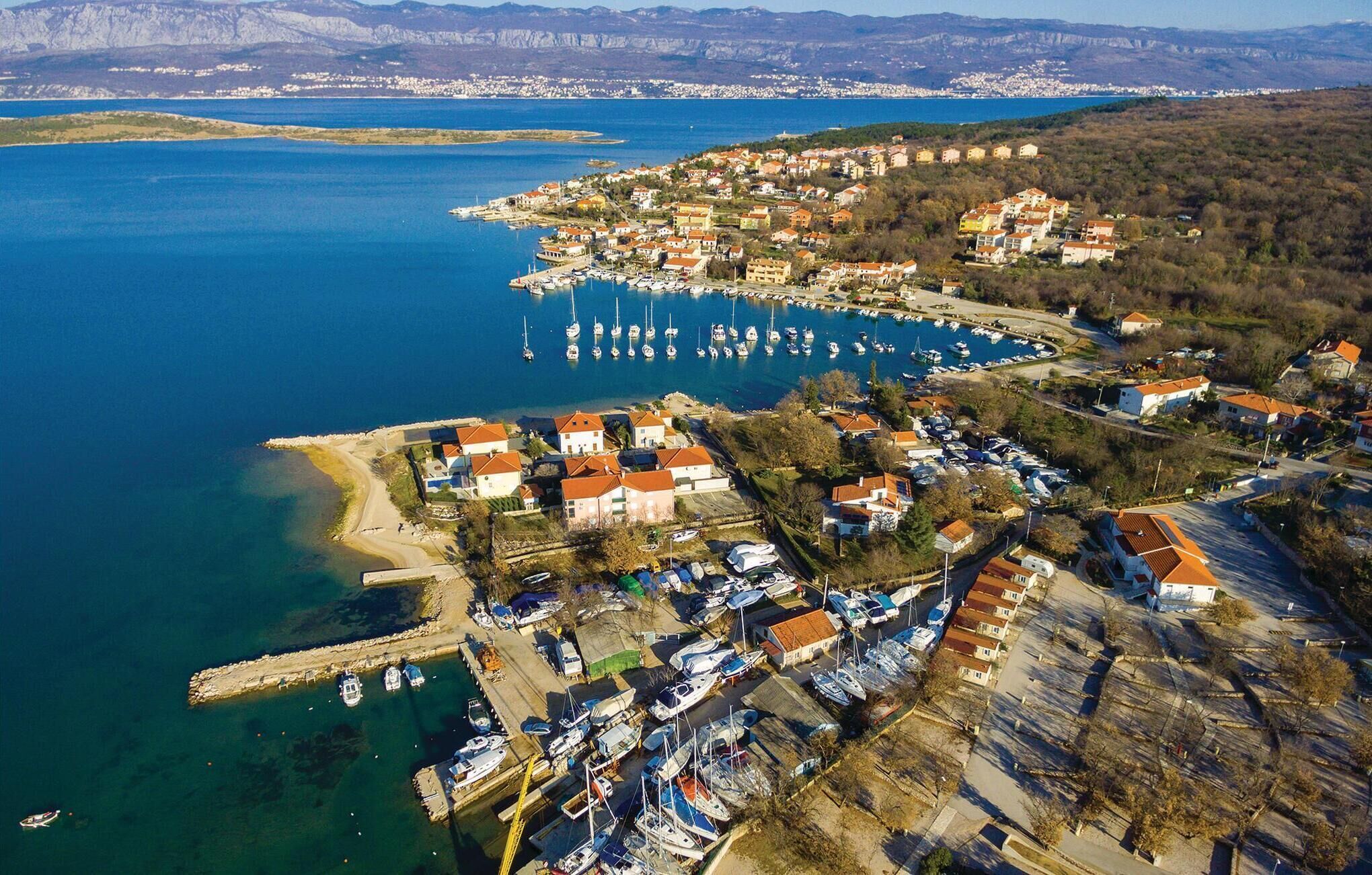 Vue aérienne d’une ville côtière avec un port de plaisance, des maisons et une chaîne de montagnes en arrière-plan.