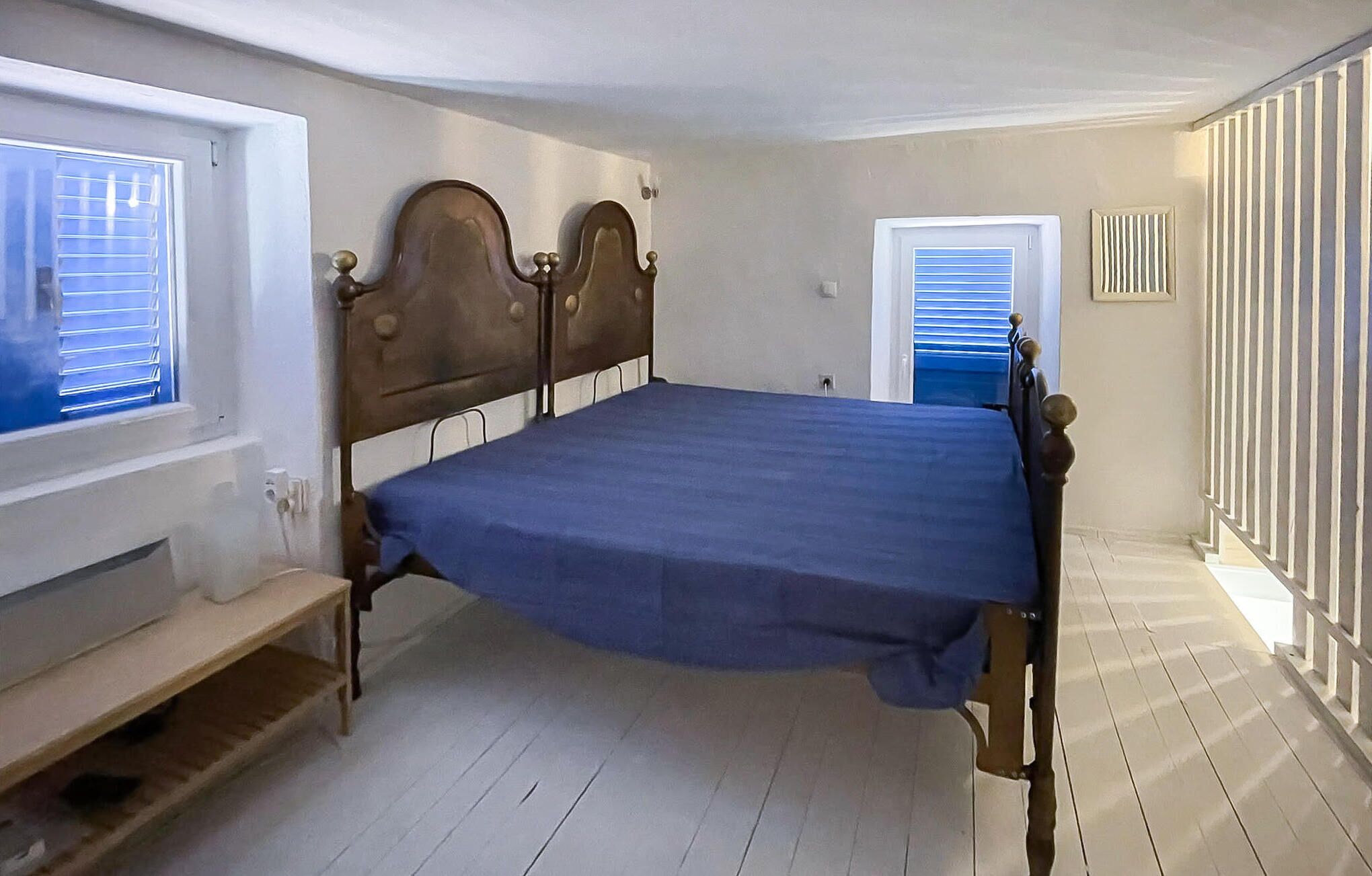 A bedroom with a wooden bed, a small bench, and a window with blinds.
