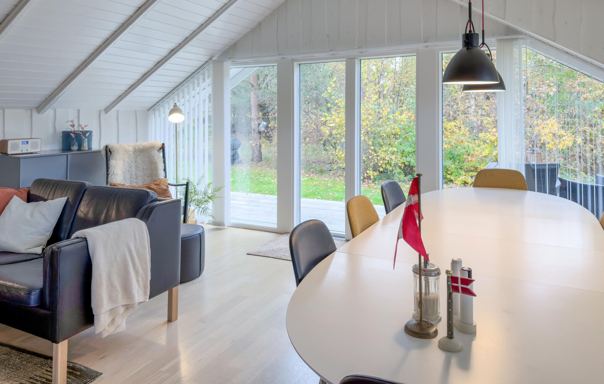 Een moderne woonkamer met een grote ronde tafel, leren banken en een uitzicht op een tuin door grote ramen.