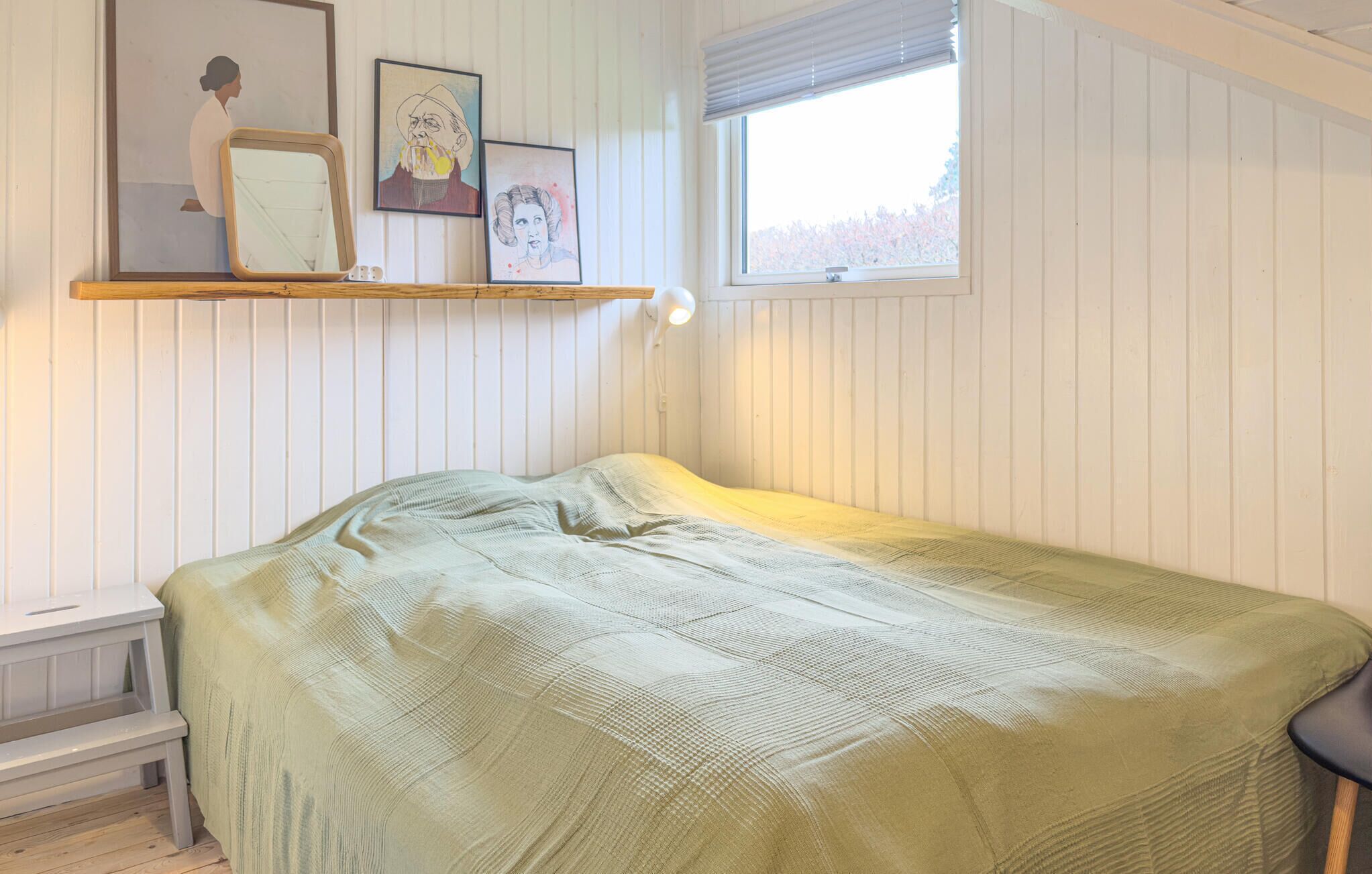 Een slaapkamer met een bed, een raam en een wandplank met ingelijste kunstwerken.