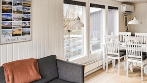 Un cuarto acogedor con un sofá gris, una mesa de comedor blanca y sillas, un ventanal con vistas, y un collage de fotos enmarcadas en la pared.