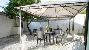 An outdoor patio area with a covered seating arrangement, including a table and chairs, surrounded by potted plants and a gravel ground. - Etesia (Vibo Valentia)