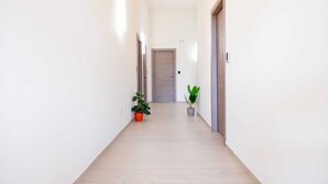 A hallway with light wooden flooring, white walls, and two potted plants. - Etesia (Vibo Valentia)