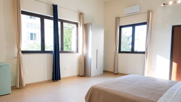A bedroom with a bed, two windows, a wardrobe, and an air conditioning unit. - Etesia (Vibo Valentia)