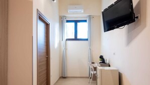 A hallway with a wooden door, a window with curtains, a desk with a chair, and a television mounted on the wall. - Etesia (Vibo Valentia)