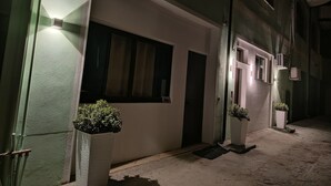 A narrow alleyway with a building featuring a large window and a door, a small potted plant, and an air conditioning unit mounted on the wall. - Etesia (Vibo Valentia)