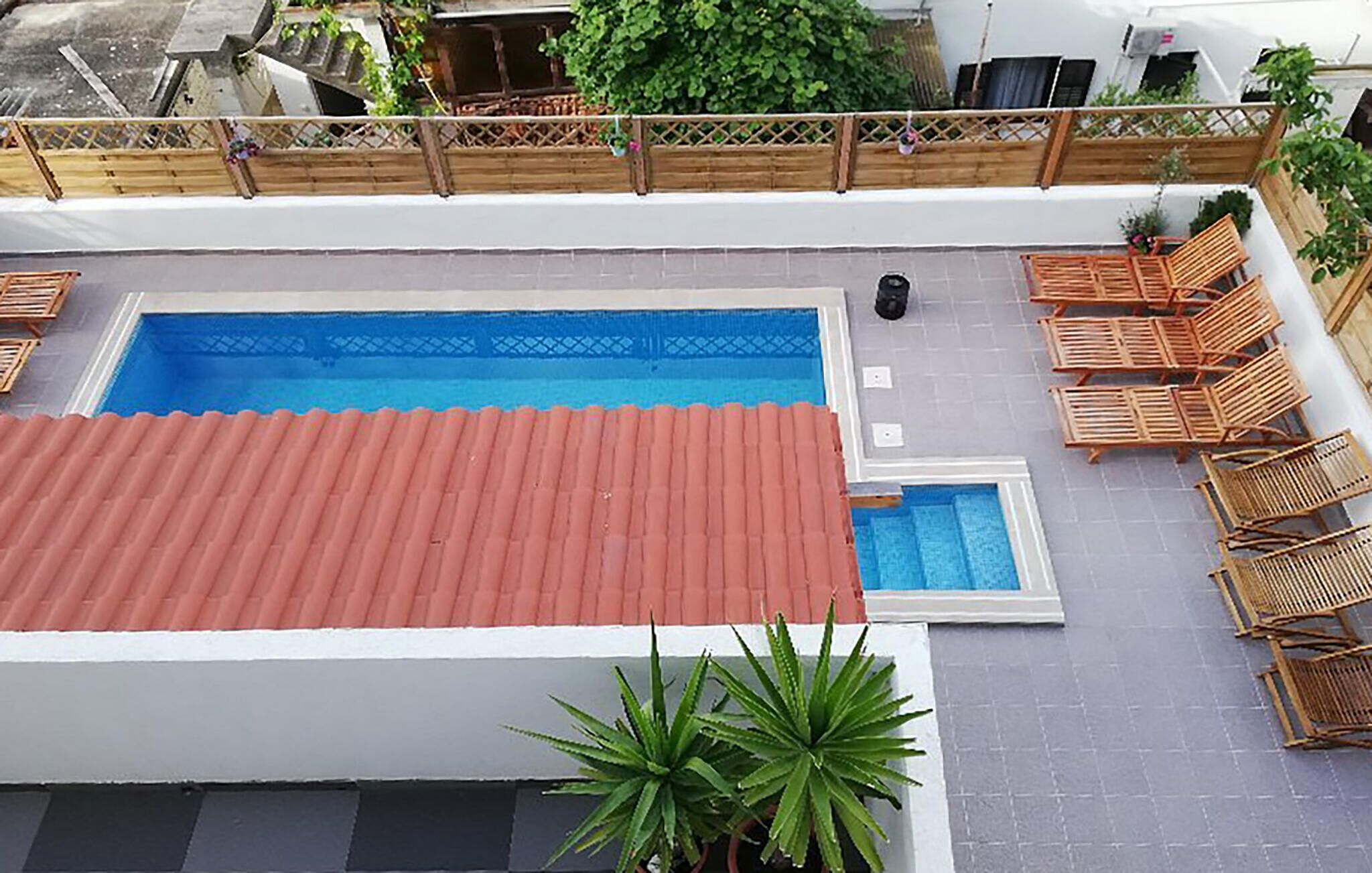 Une piscine sur le toit, surmontée d’un toit rouge, entourée de chaises longues en bois et délimitée par une clôture en bois.