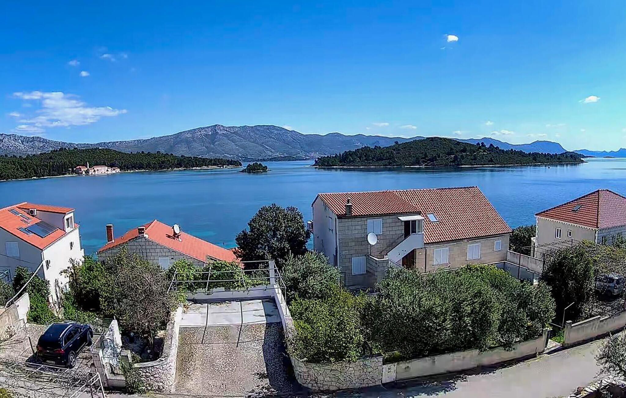 Ein Küstendorf mit traditionellen Steinbauten, einem klaren, blauen See und Bergen im Hintergrund.
