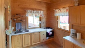 Eine kleine Küche mit Holzausstattung, einer Spüle, einem Herd und einem Fenster mit Vorhängen.