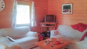 Ein gemütliches Wohnzimmer mit zwei weißen Sofas, einem Holztisch, einem Fernseher auf einem Schrank und einem Bild an der Wand.