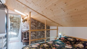 A bedroom with a wooden ceiling, a bed with floral bedding, a bedside table, a nightstand, and a window with a view of a tropical landscape. - Casa Matiri by Wonderful Italy (Catania)