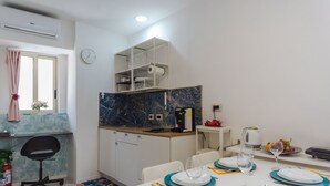 A modern kitchen with a marble backsplash, white cabinets, and a built-in microwave. There is a dining area with a white table set for four, blue plates, and a clock on the wall. - Casa Matiri by Wonderful Italy (Catania)