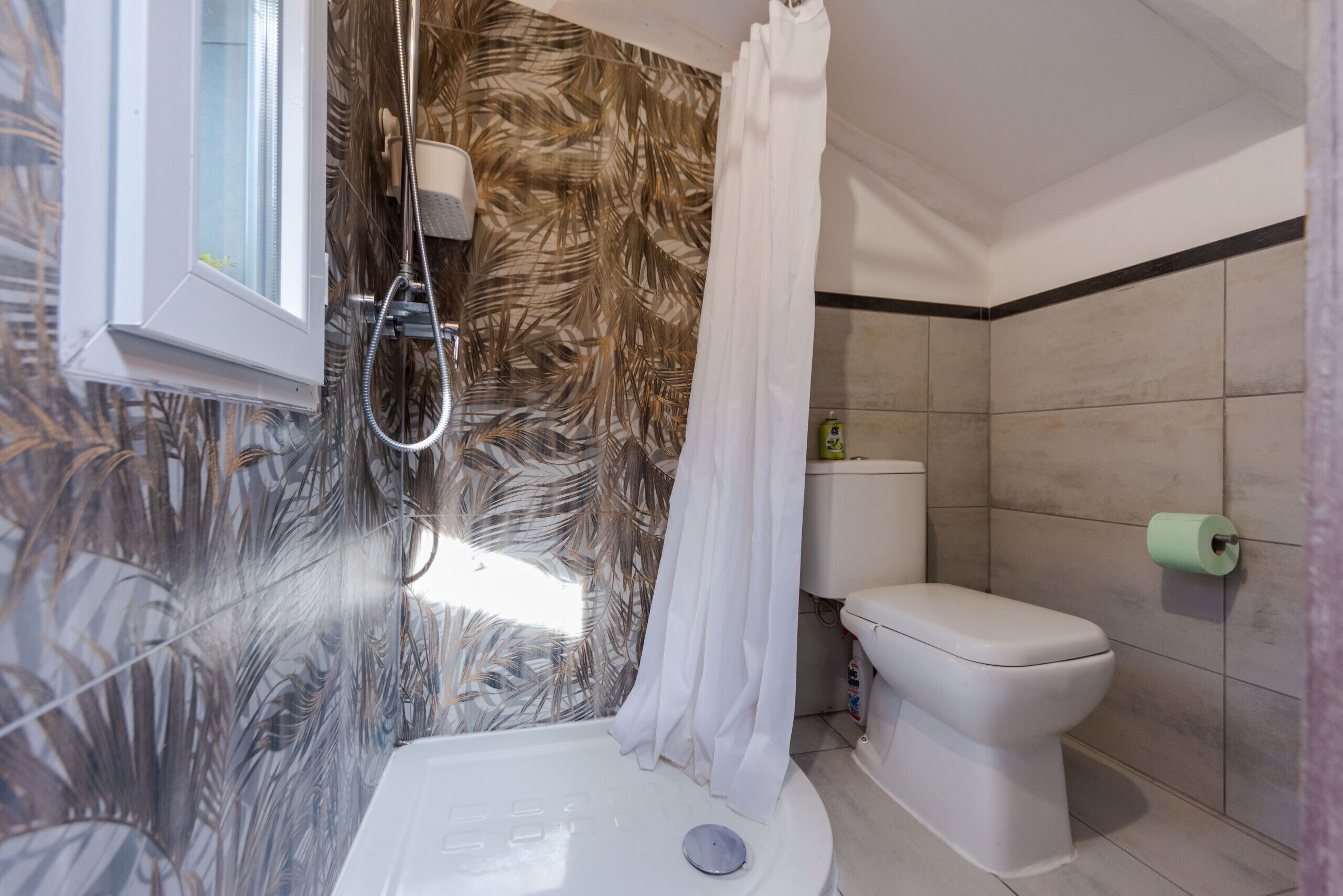 A modern bathroom with a shower, toilet, and a window.