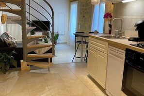 A modern kitchen with a built-in dishwasher, a dining area with a table and chairs, and a spiral staircase leading to another level. - Gîte confort at Lamothe d'alès (Lavergne)