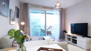 Un soggiorno moderno con televisore a schermo piatto, un divano, un tavolino da caffè e un balcone con mobili in rattan.