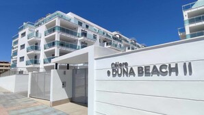 Ein modernes Mehrgeschosshaus mit Balkonen, einem verschlossenen Eingang und einem Schild mit der Aufschrift 'Céline BUNA BEACH II'.