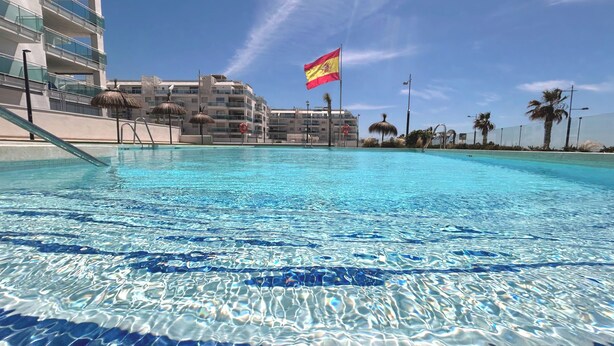Ein klares Schwimmbecken mit einer Flagge, moderne Gebäude und Palmen.