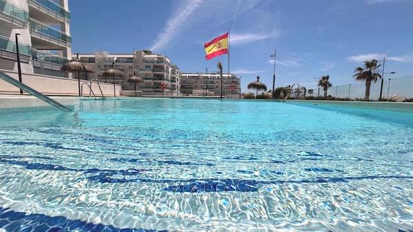 Ein klares Schwimmbecken mit einer Flagge, moderne Gebäude und Palmen.