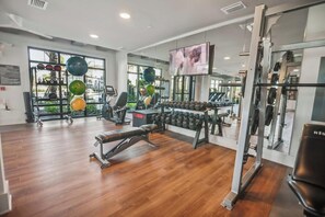 A gym with exercise equipment, a bench, and a television screen. - Landing | Beautiful 1BD, Gym, Clubhouse (Wimauma)