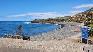 A coastal beach with a stone pathway leading to a wooden boardwalk, a rocky shoreline, and a signboard. - Apartamento vista Mar Caleta de Interián - Casa Oceano (La Caleta de Interián)